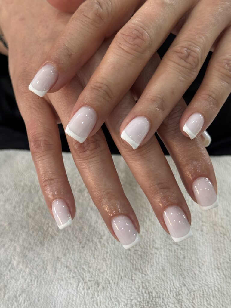 Vista de manos con baño de acrílico sobre uña natural y diseño de manicura francesa clásica